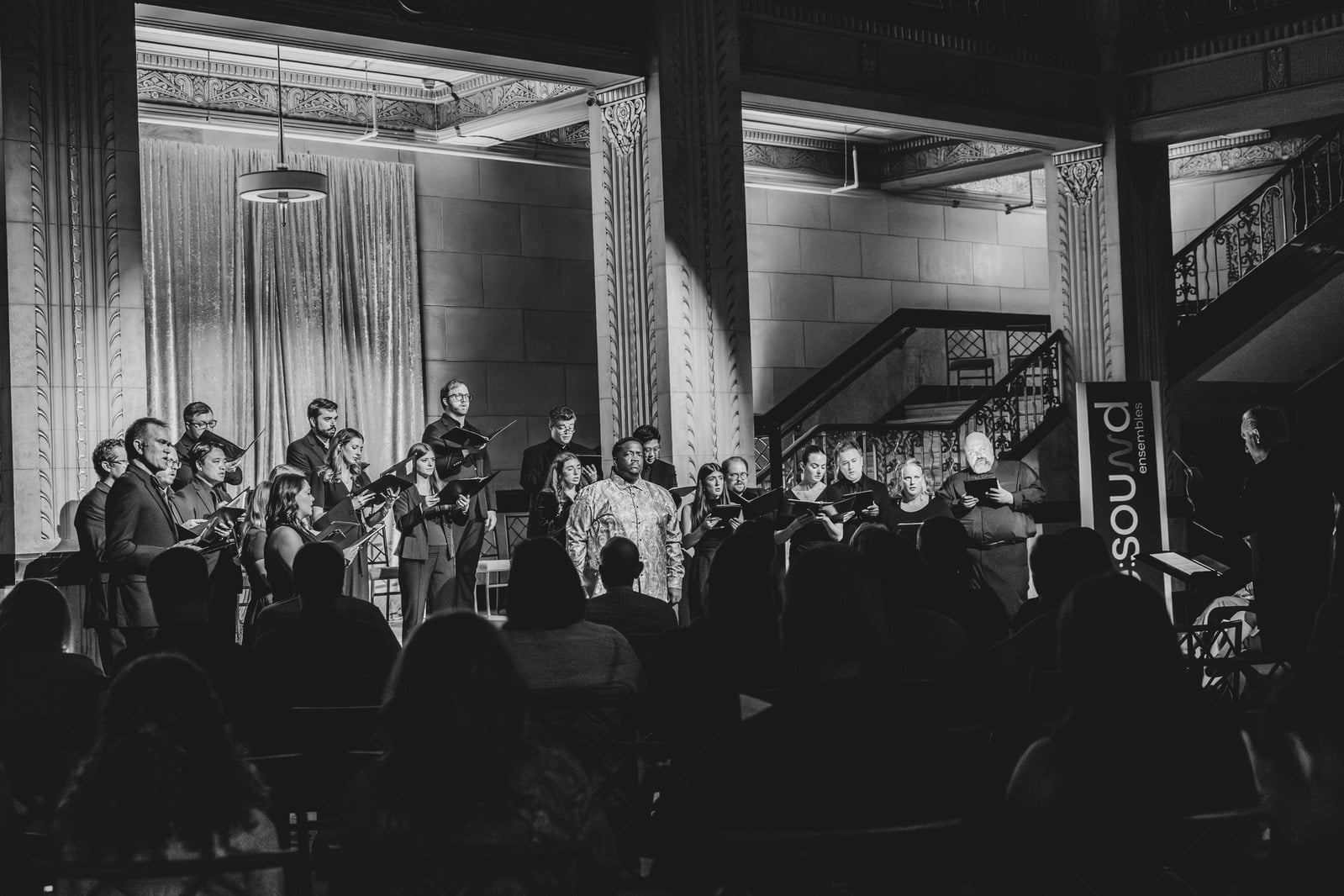 Wide black-and-white choir shot with conductor silhouette